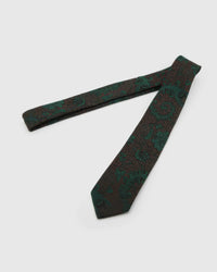 Emerald Baroque Scroll Tie laid full length on white, showing a dark brown-black ground with large emerald baroque scrolls and botanical flourishes from blade to tail.