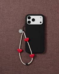 Scarlet Heart beaded phone strap attached to a black phone case, showing three glossy red hearts against silver-tone beads.