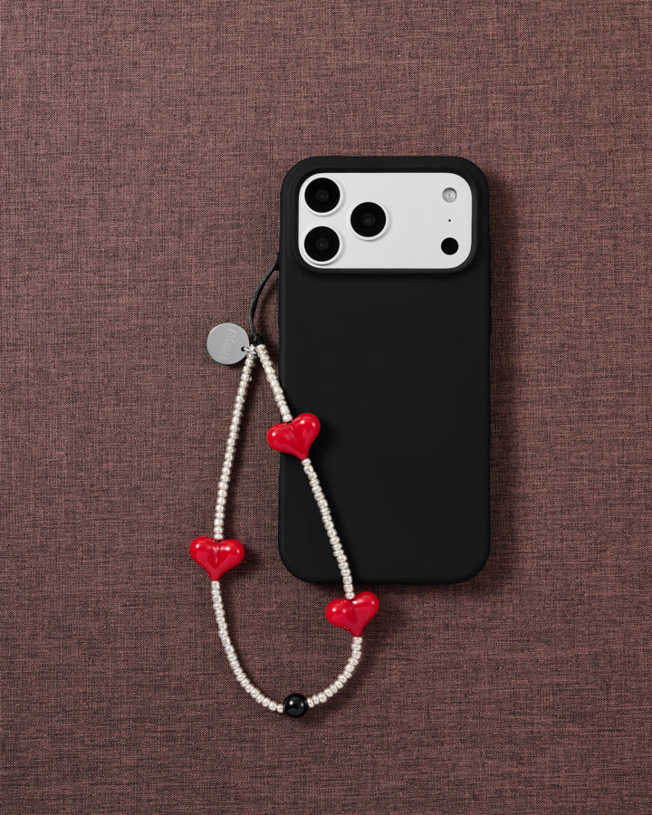 Scarlet Heart beaded phone strap attached to a black phone case, showing three glossy red hearts against silver-tone beads.