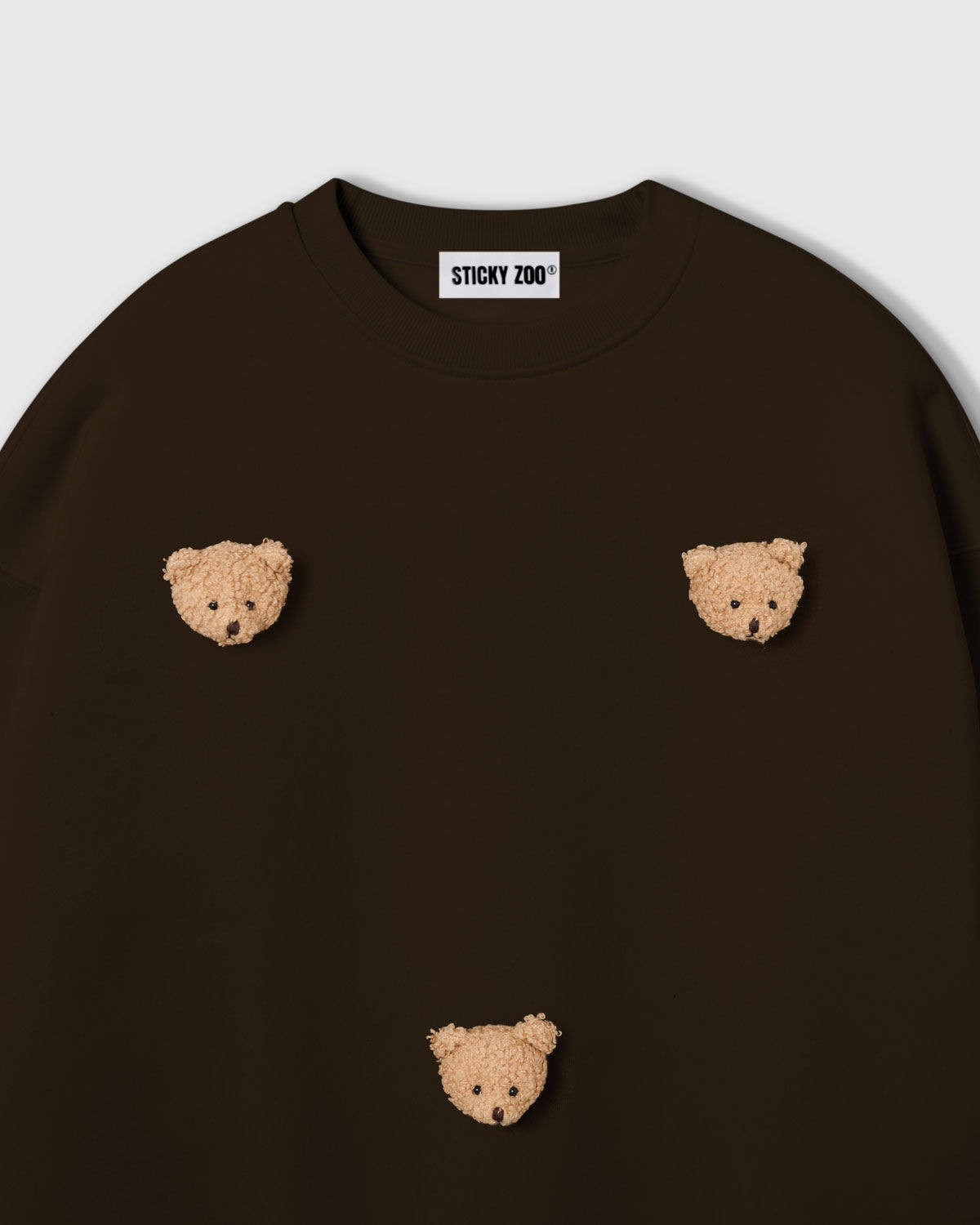 Detail of scattered plush teddy bear faces on STICKYZOO brown sweatshirt showing handmade craft