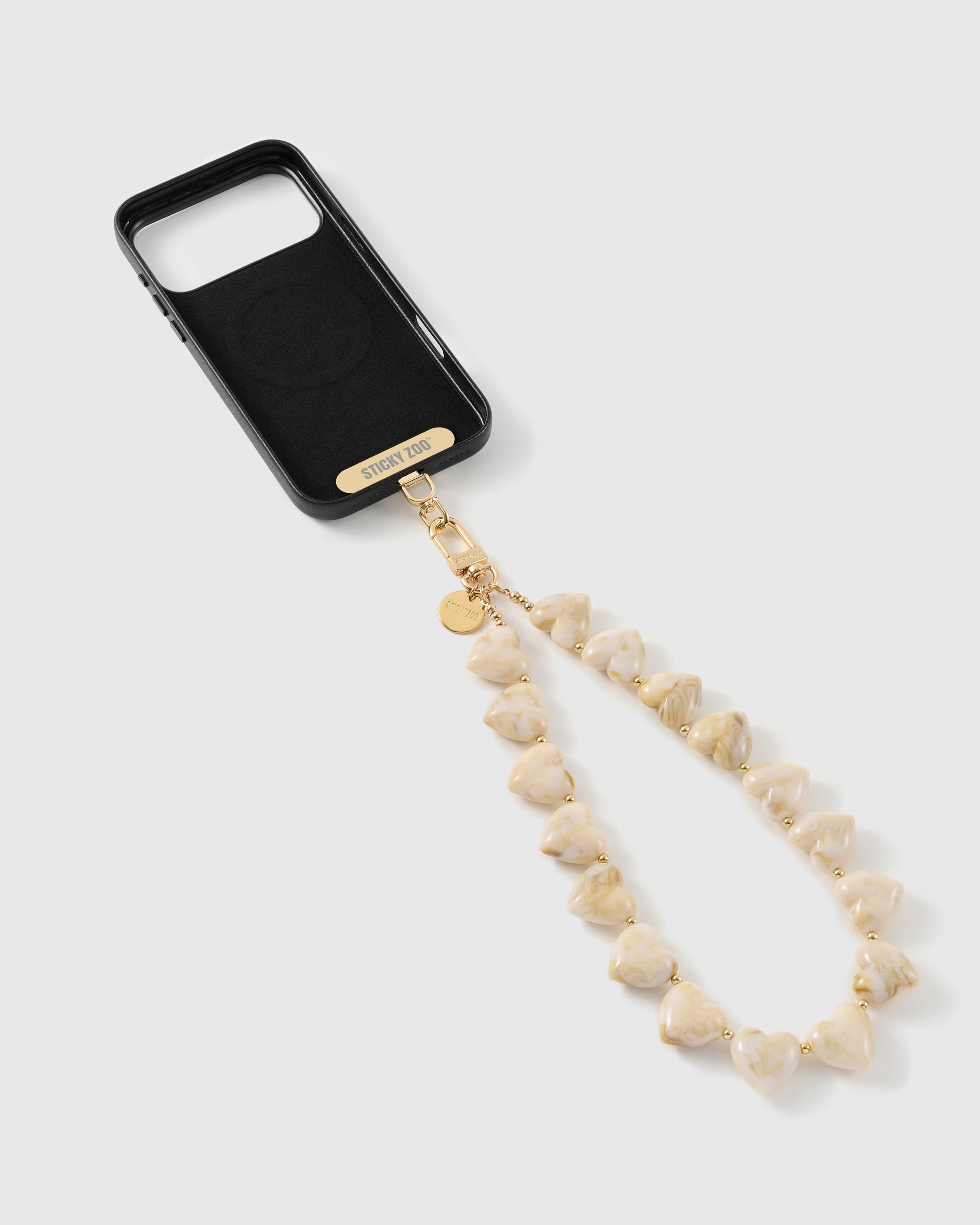 Black phone case with a gold STICKYZOO strap card and clasp, joined to a strand of marbled ivory heart beads with gold-tone spacers.