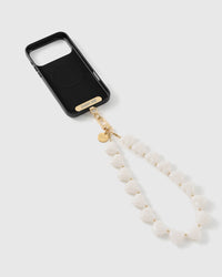 Milky white heart bead strap on a black phone, attached with a gold STICKYZOO connector plate and engraved disc.