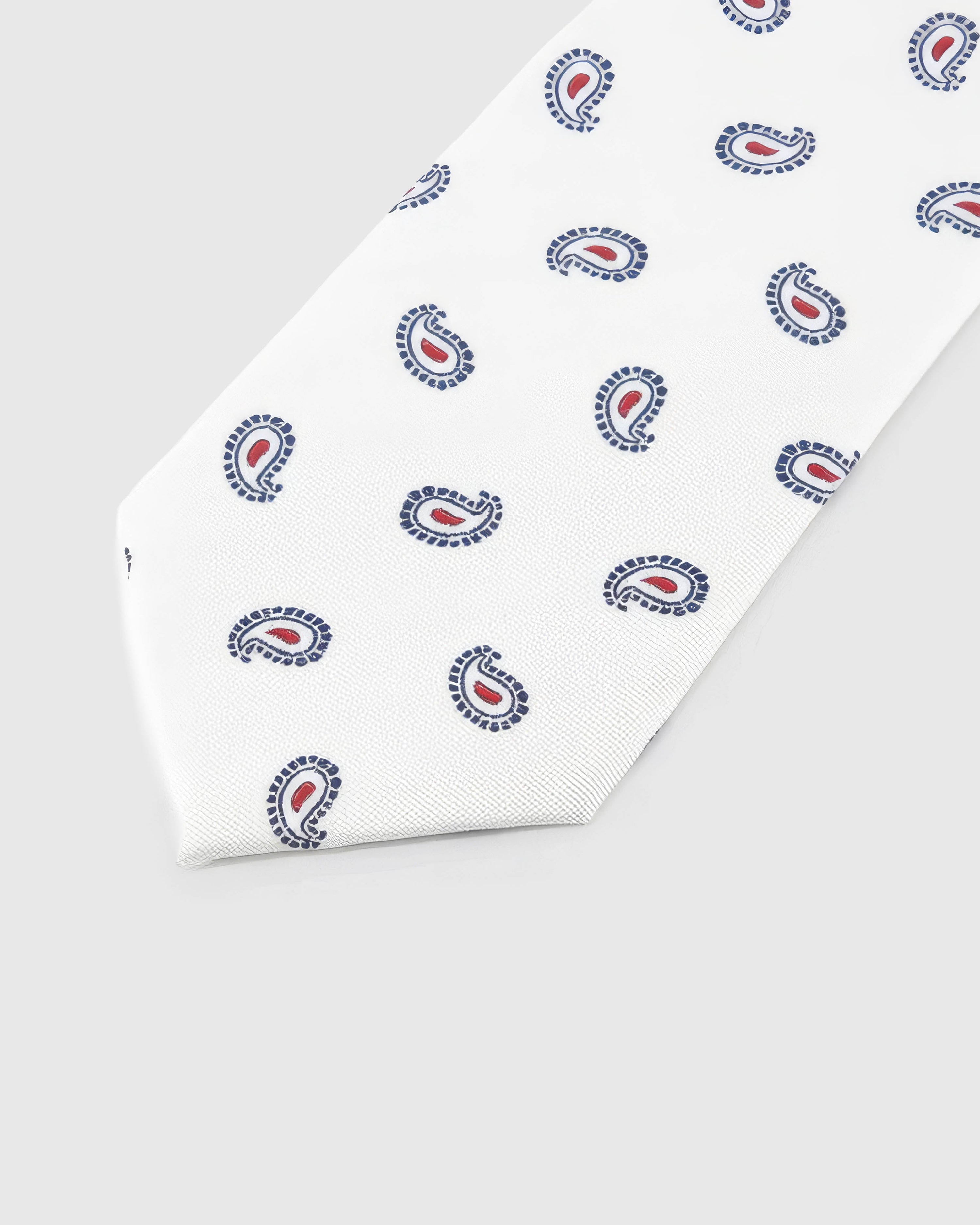 Ivory Tricolor Paisley Tie detail showing navy-outline paisley with crimson centres, raised thread and the tactile ivory silk surface.