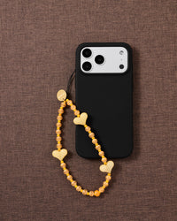 Apricot Heart beaded phone strap attached to a black phone case, showing three glossy yellow hearts and striped beads.