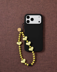 Lemon Heart beaded strap looped onto a black phone case on mauve fabric, pale yellow hearts and striped beads hanging free