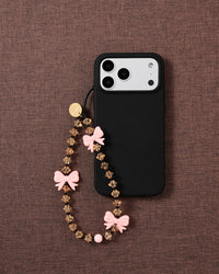 STICKYZOO bow strap looped onto a black phone case on mauve fabric, showing honey beads, black spacers and a round pink bead