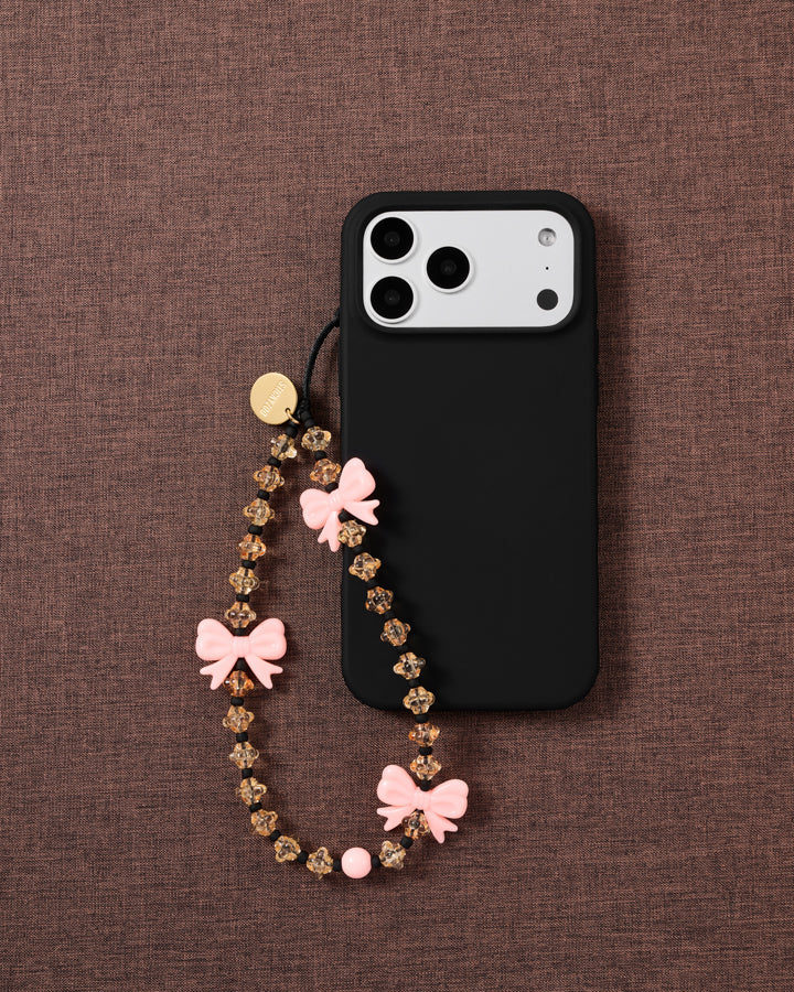 STICKYZOO bow strap looped onto a black phone case on mauve fabric, showing honey beads, black spacers and a round pink bead