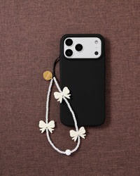 Ivory Bow faux-pearl phone strap attached to a black phone case with all three bow details visible.