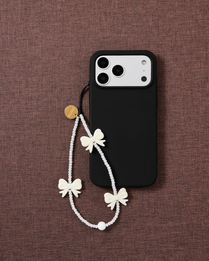 Ivory Bow faux-pearl phone strap attached to a black phone case with all three bow details visible.