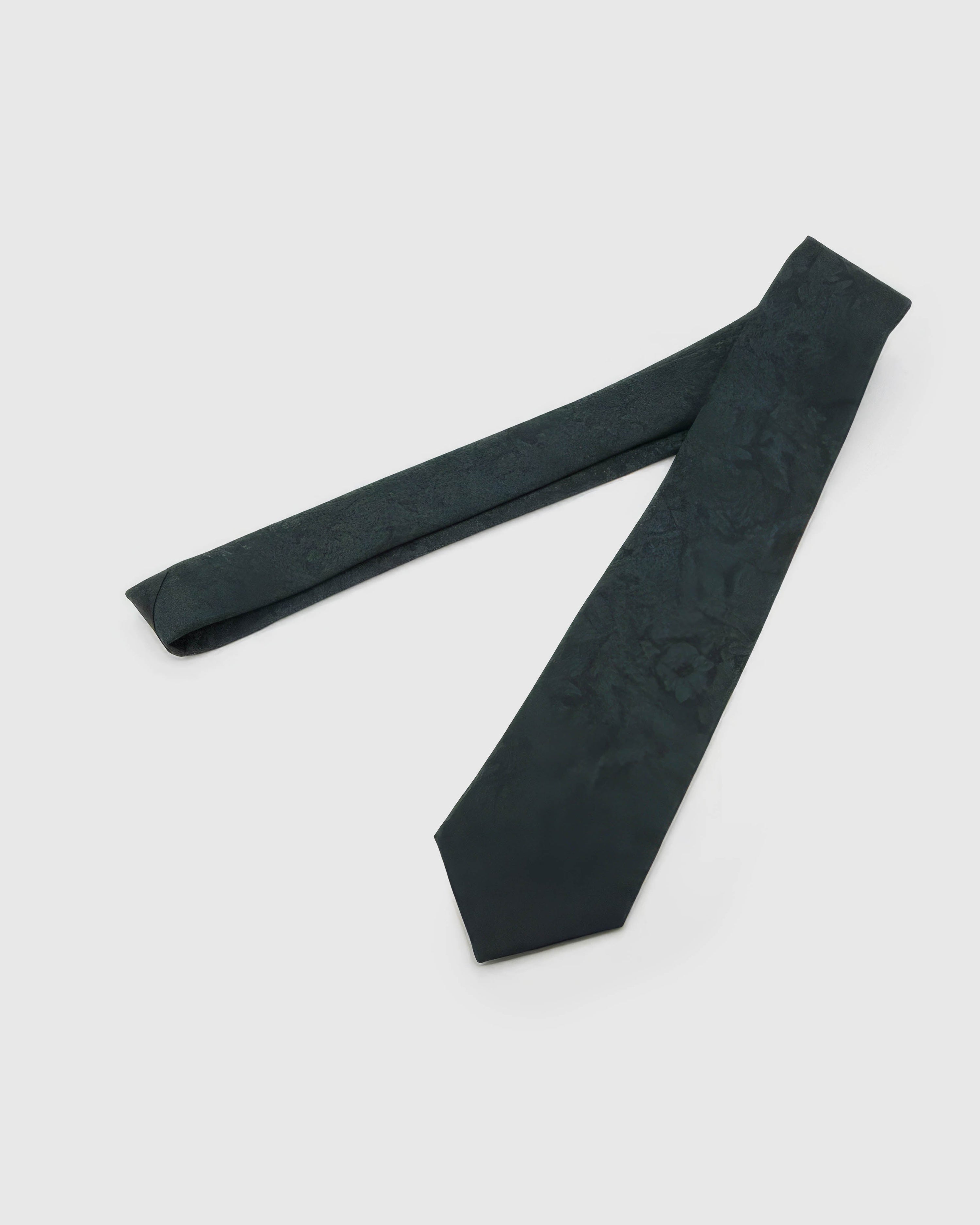 Forest Shadow Floral Tie laid full length on white, showing a low-contrast forest-teal field of shadowed florals and abstract foliage from blade to tail.