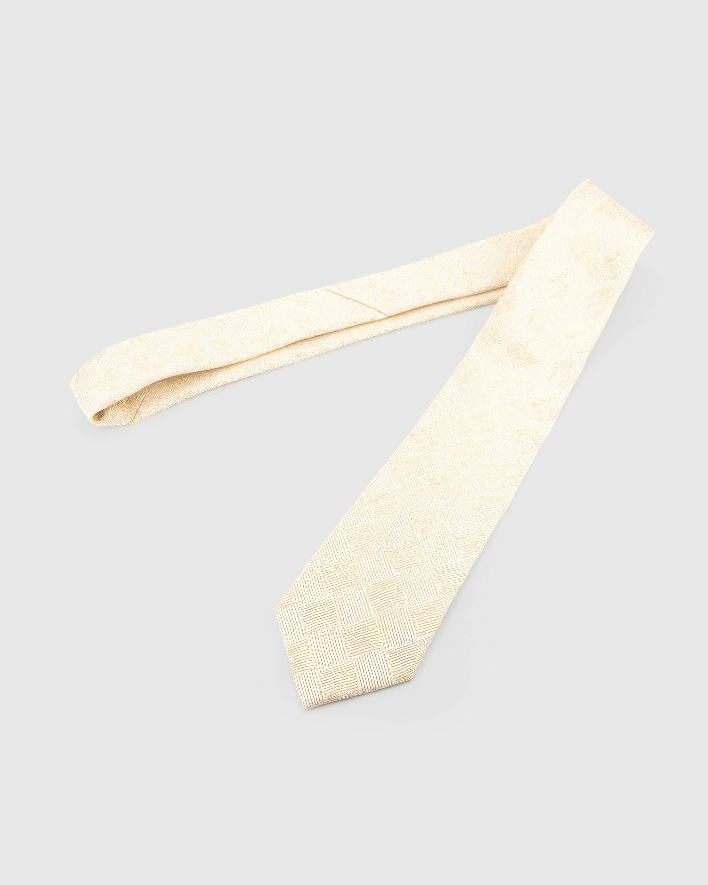 Ivory Gilded Grid Tie laid full length on white, showing an ivory field crossed by a pale-gold, softly irregular grid from blade to tail.