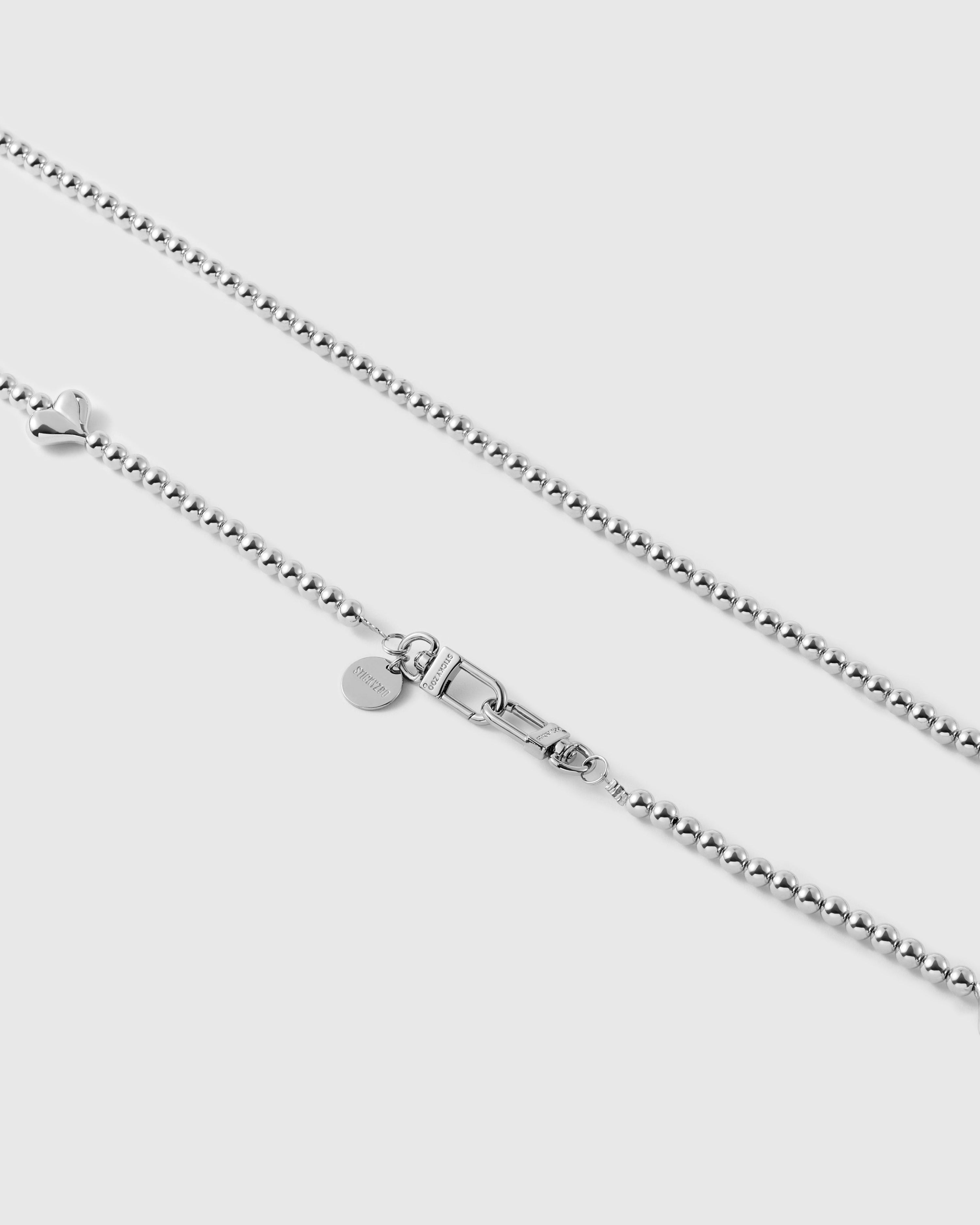 Close view of a puffy silver-tone heart, ball-bead chain, dual clasp and engraved STICKYZOO disc.