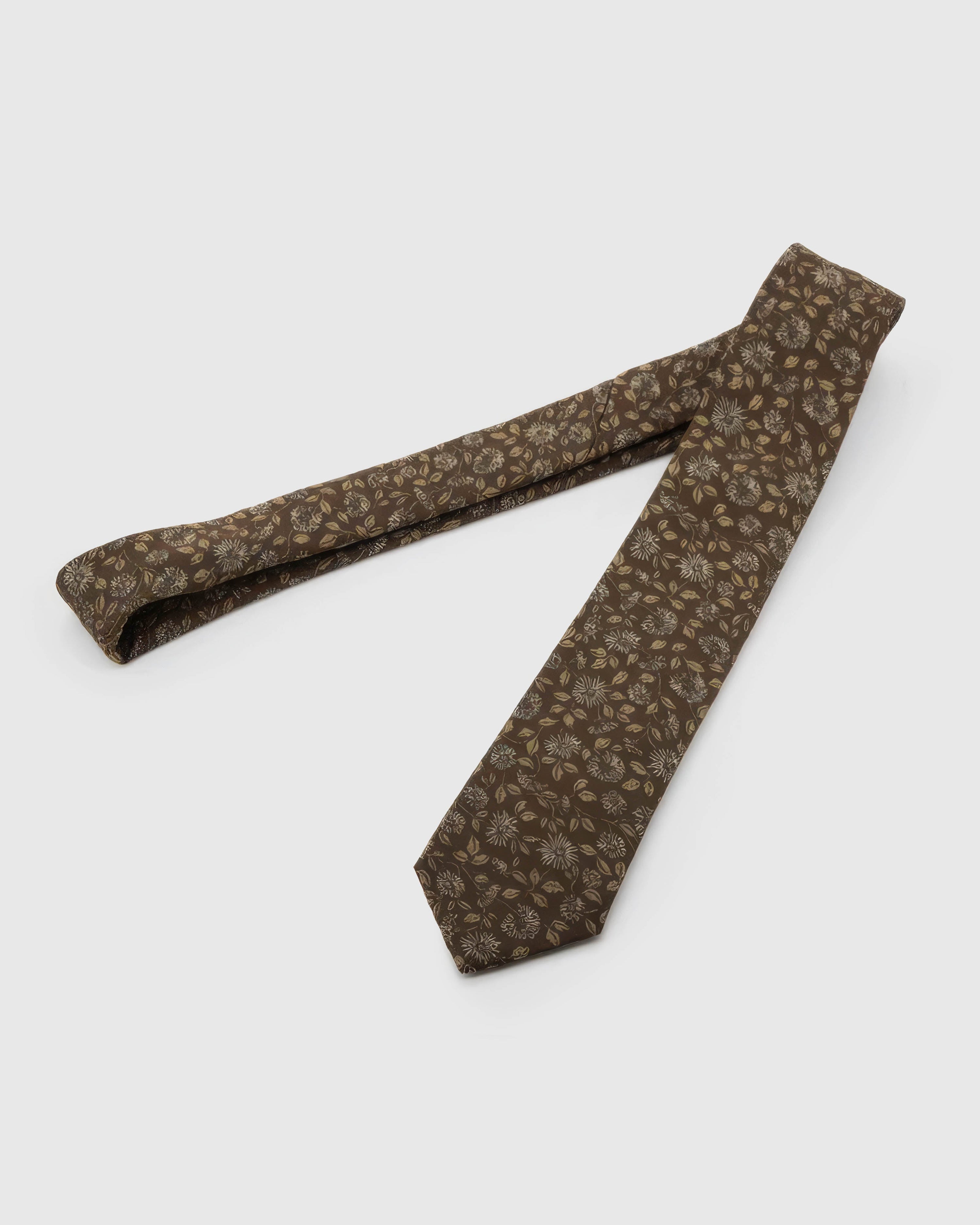 Espresso Ivory Bloom Tie laid full length on white, showing an espresso ground with ivory flowers, muted-gold petals, and soft botanical leaves from blade to tail.