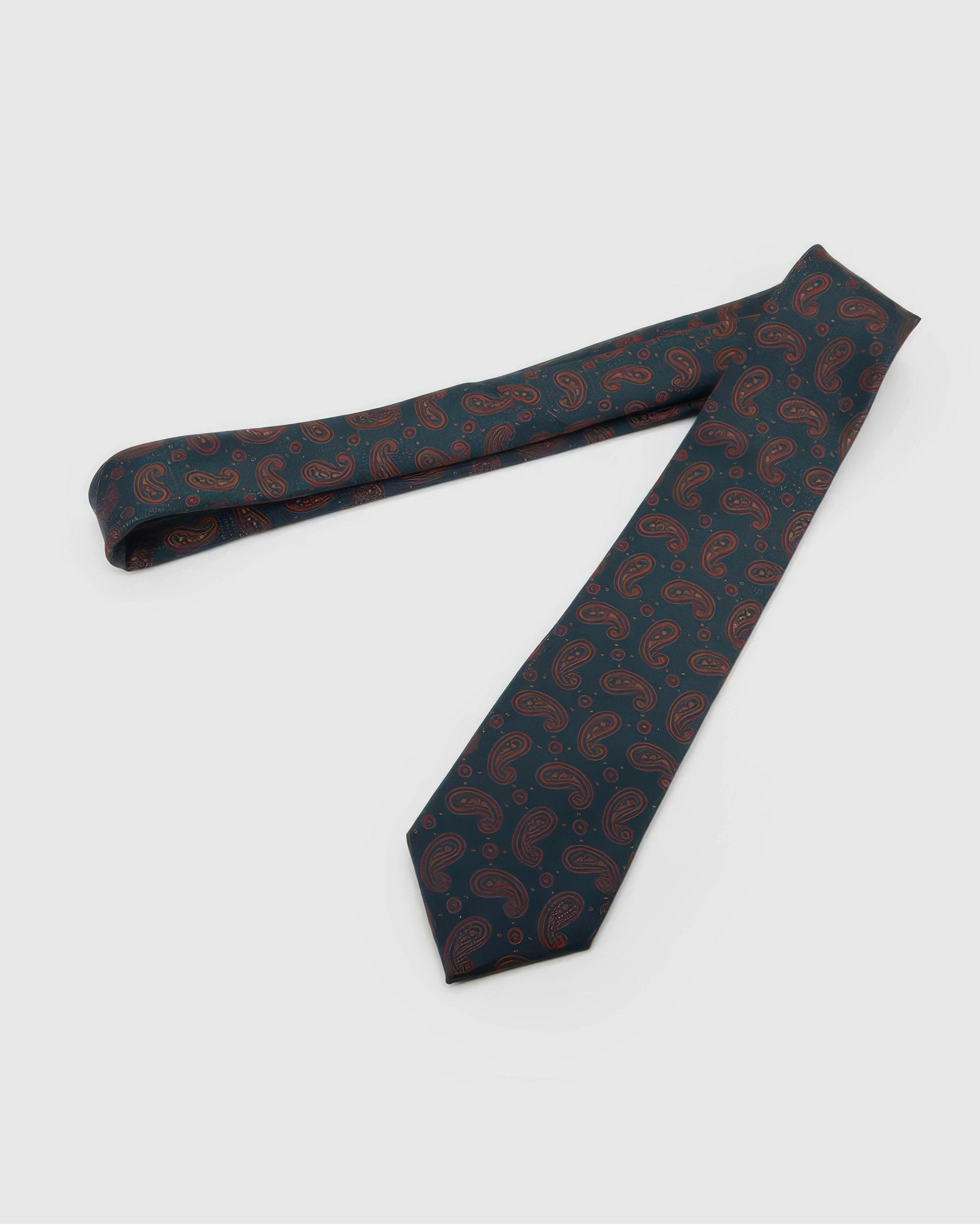 Petrol Copper Paisley Tie laid full length on white, showing a deep petrol ground covered in a fine copper-outline paisley repeat from blade to tail.