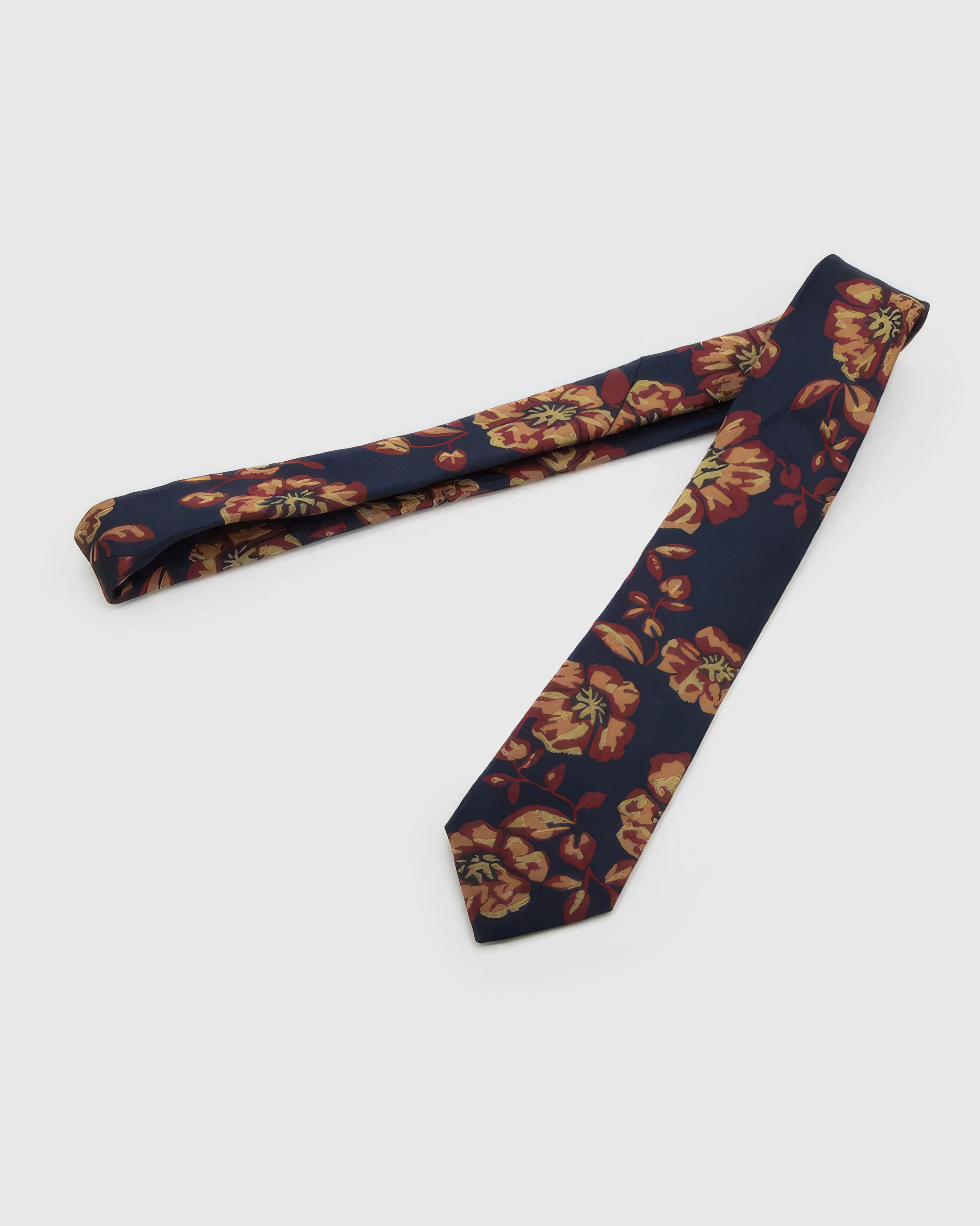 Navy Gilded Bloom Tie laid full length on white, showing a navy ground with large burgundy-red and gilded botanical blooms from blade to tail.
