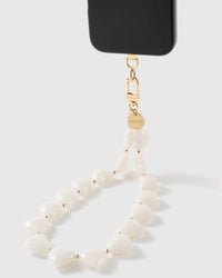 Milky white heart bead strap clipped to a black phone, showing the 18K gold-plated hook and STICKYZOO-engraved disc up close.