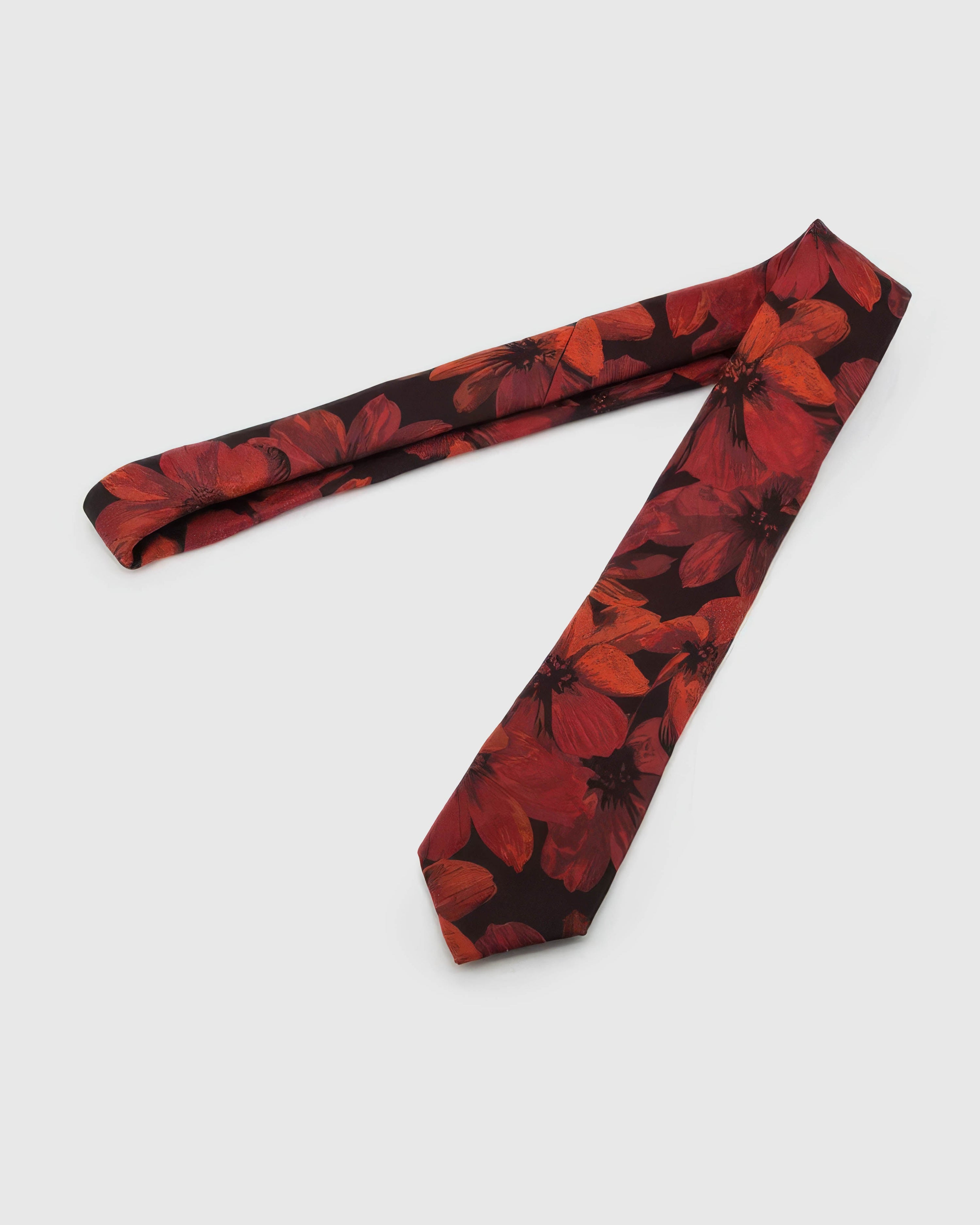 Oxblood Scarlet Bloom Tie laid full length on white, showing an oxblood ground carrying vivid scarlet botanical blooms and dark leaves from blade to tail.
