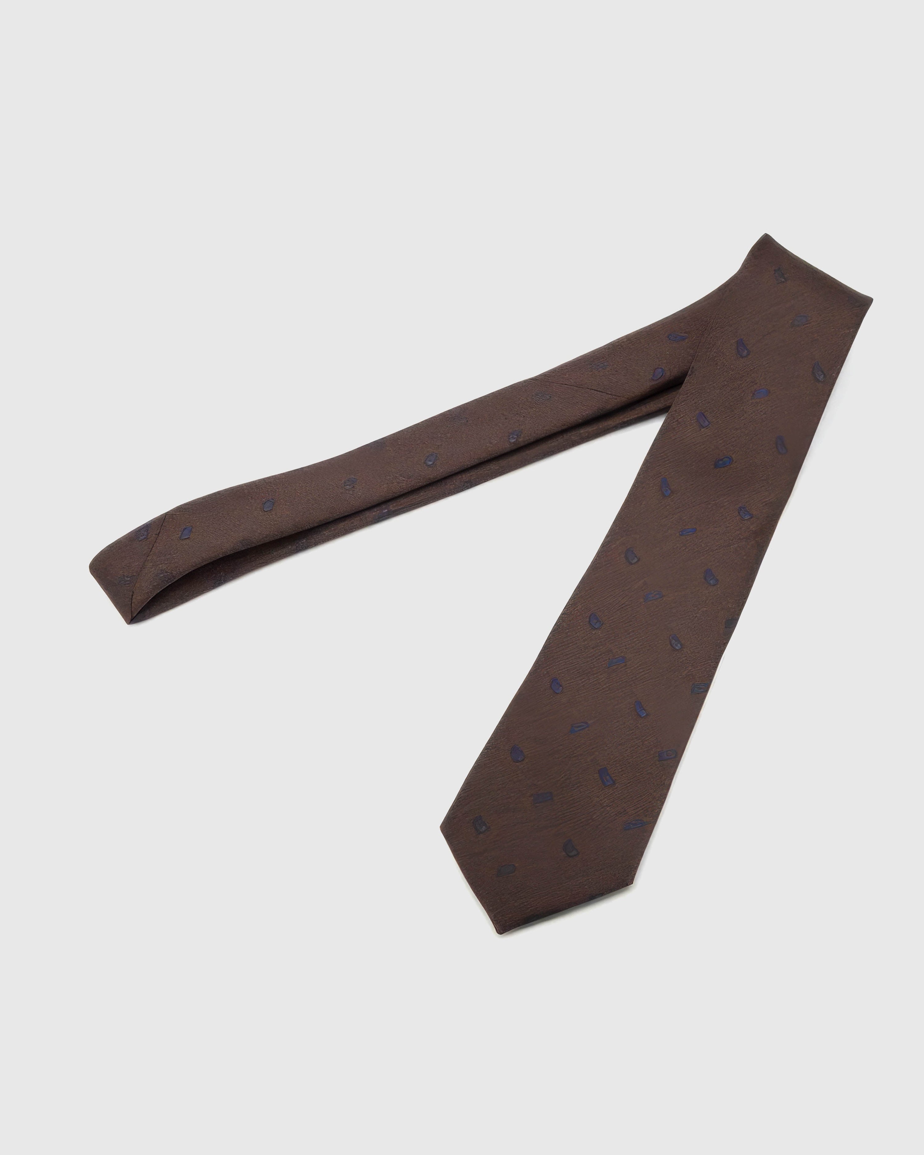 Espresso Sapphire Paisley Tie laid full length on white, showing a textured espresso ground with a compact sapphire-blue paisley repeat from blade to tail.