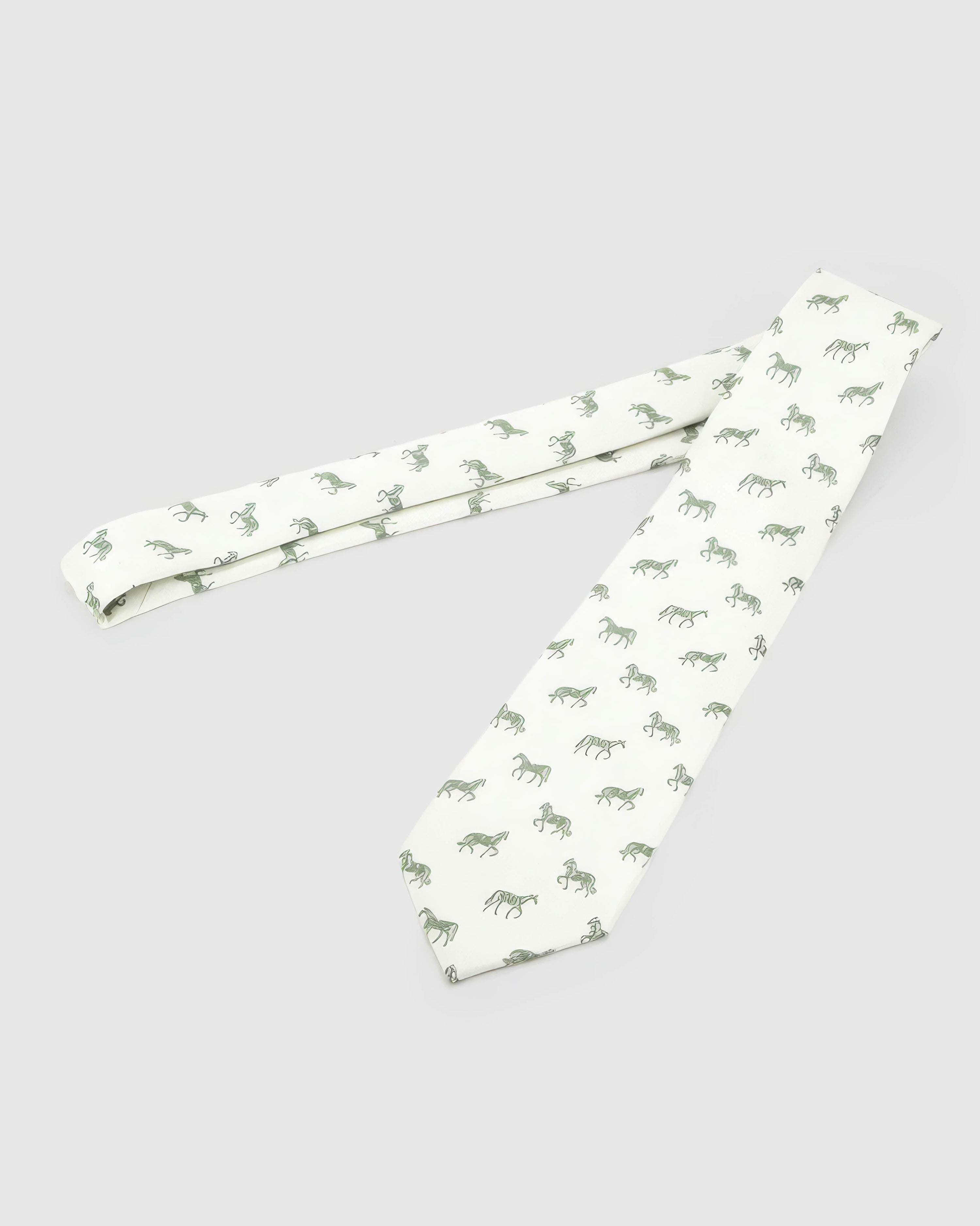 Ivory Equestrian Tie laid full length to show ivory ground with sage and forest horse silhouettes from blade to tail.