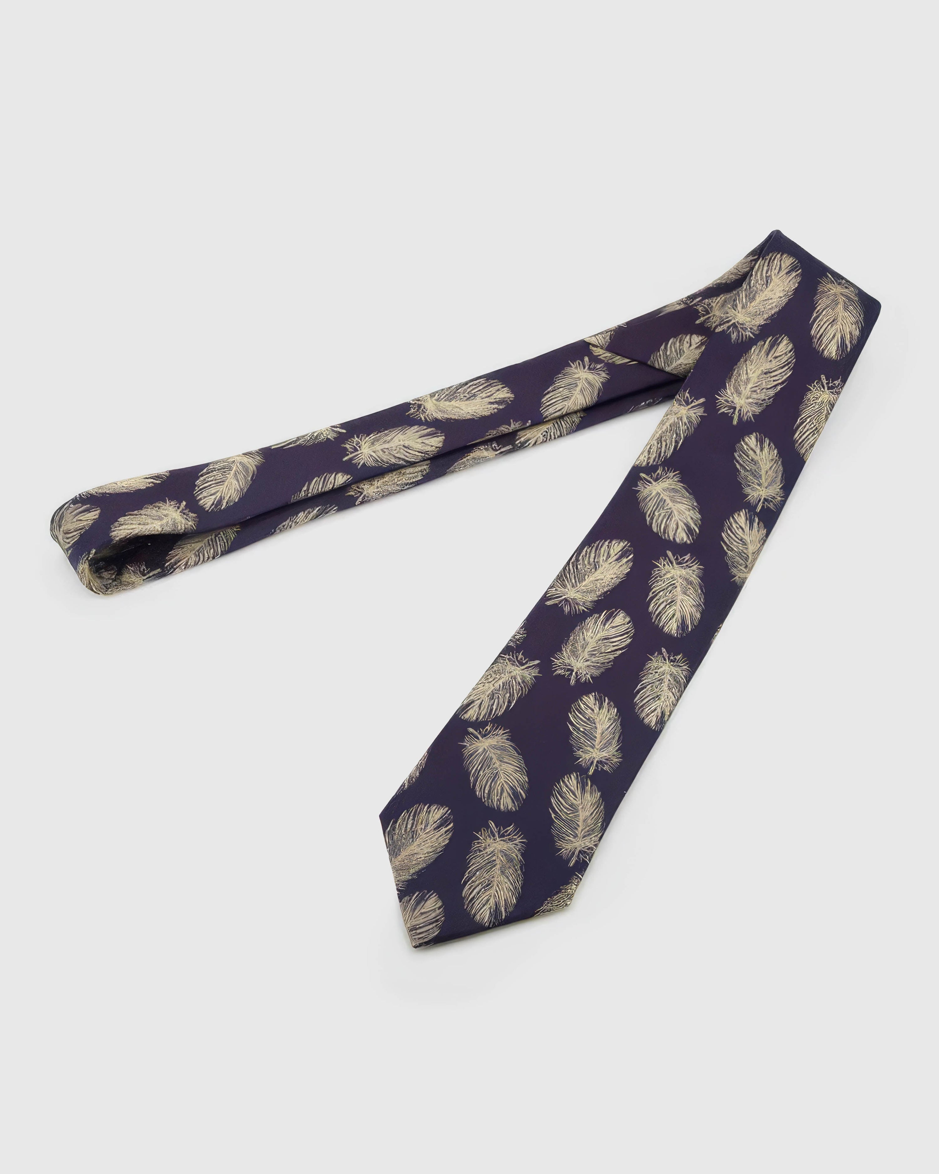 Aubergine Gilded Feather Tie laid full length on white, showing a deep aubergine ground scattered with slender pale-gold feathers from blade to tail.