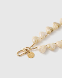 Close-up of the gold hook, engraved STICKYZOO disc and the beige marbled veining across the ivory heart beads with gold-tone spacers.
