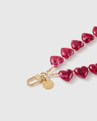 Close-up of the 18K gold-plated hook, engraved disc and gold spacer beads set between glossy ruby-red marbled heart beads.