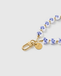 Close-up of the 18K gold-plated hook, engraved STICKYZOO disc and blue-floral porcelain heart beads — each one printed