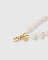 Close-up of the gold oval clasp and round STICKYZOO disc beside glossy milky white heart beads and small gold ball spacers.