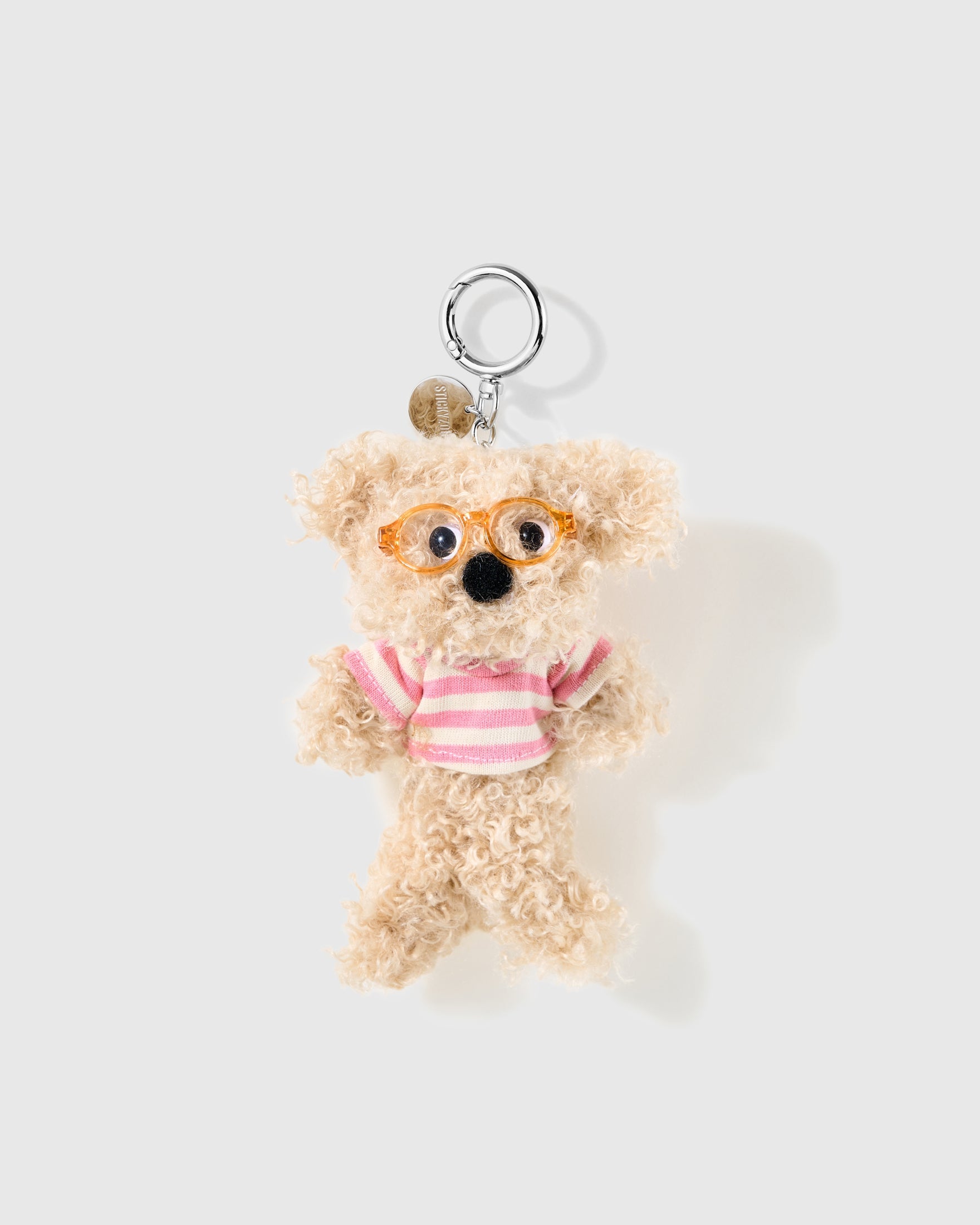 Pink Stripe Poodle Plush Charm with round glasses, shaggy tan texture and a pink-and-white top give the small character a cheerful outfit on a light background