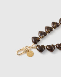 Macro of the amber-and-cocoa marbling swirling through the glossy heart beads beside the engraved gold-tone clasp and disc.