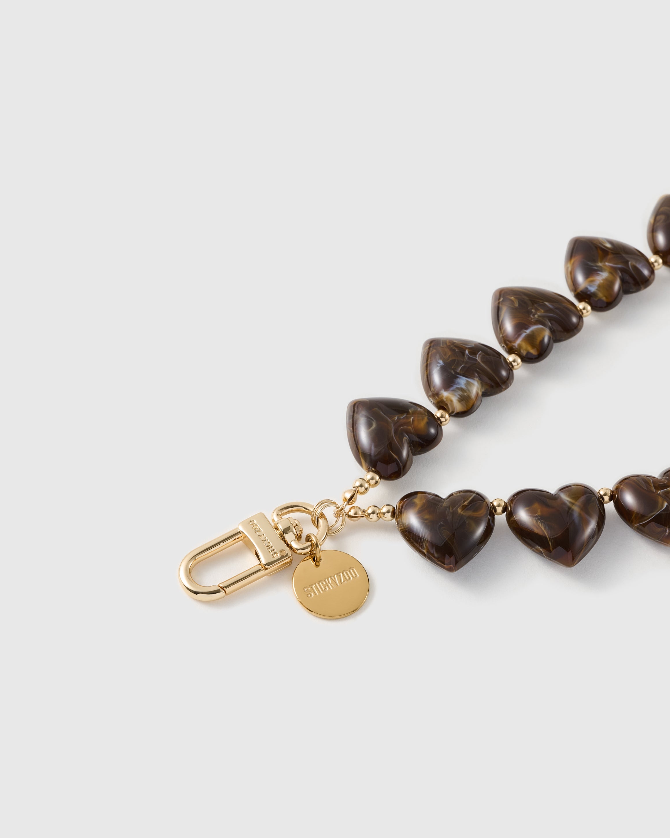 Macro of the amber-and-cocoa marbling swirling through the glossy heart beads beside the engraved gold-tone clasp and disc.