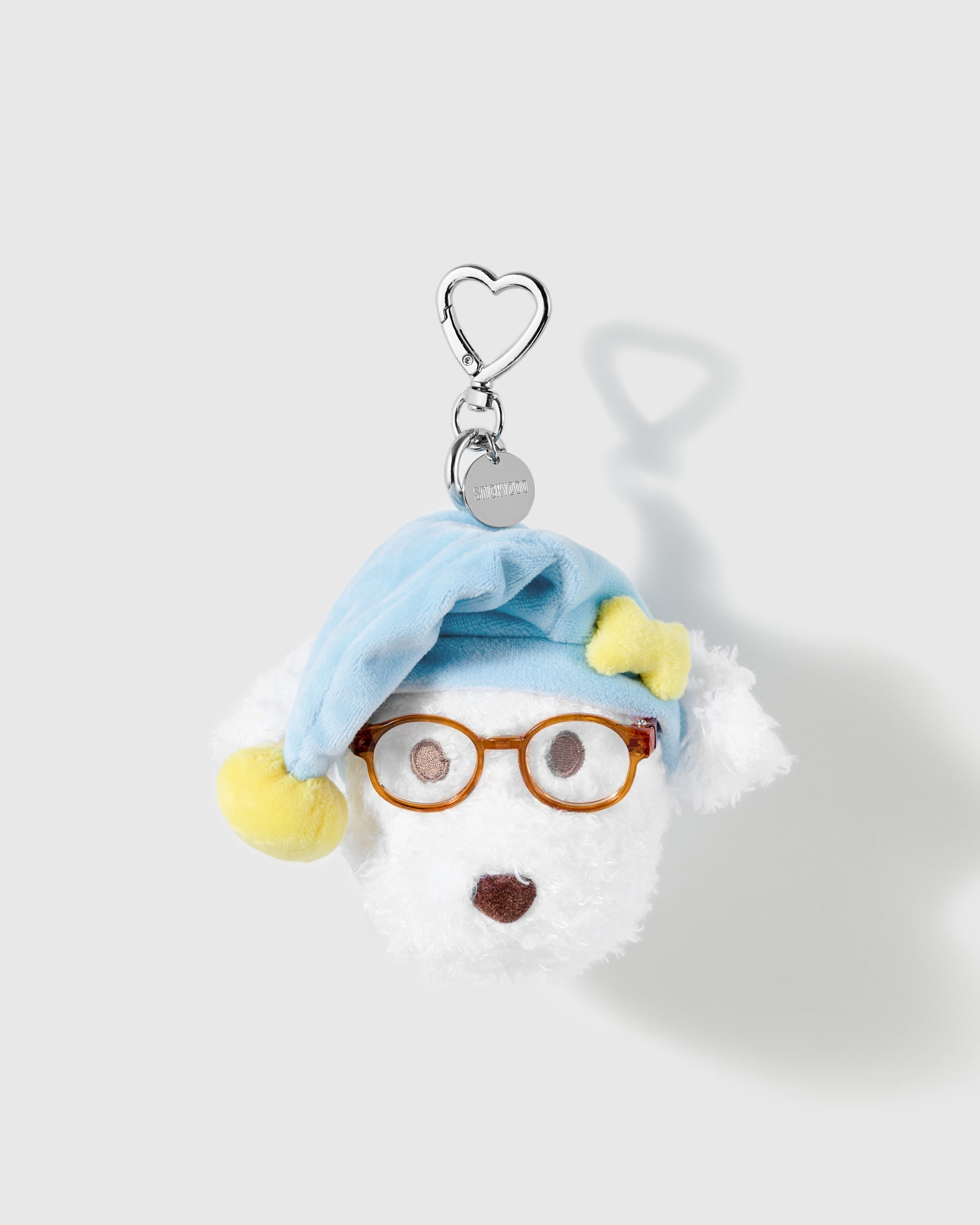 Blue Nightcap Poodle Plush Charm with round glasses, a pale blue hat and yellow pom-pom create a sleepy, bookish expression on a light background