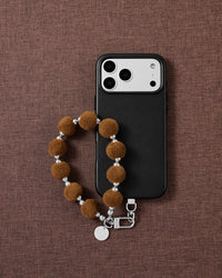 Hazelnut velvet pom phone strap styled on fabric, loved by thousands of STICKYZOO customers
