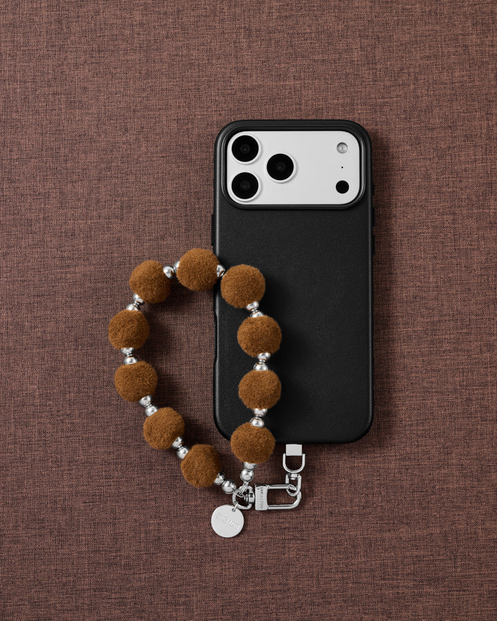 Hazelnut velvet pom phone strap styled on fabric, loved by thousands of STICKYZOO customers