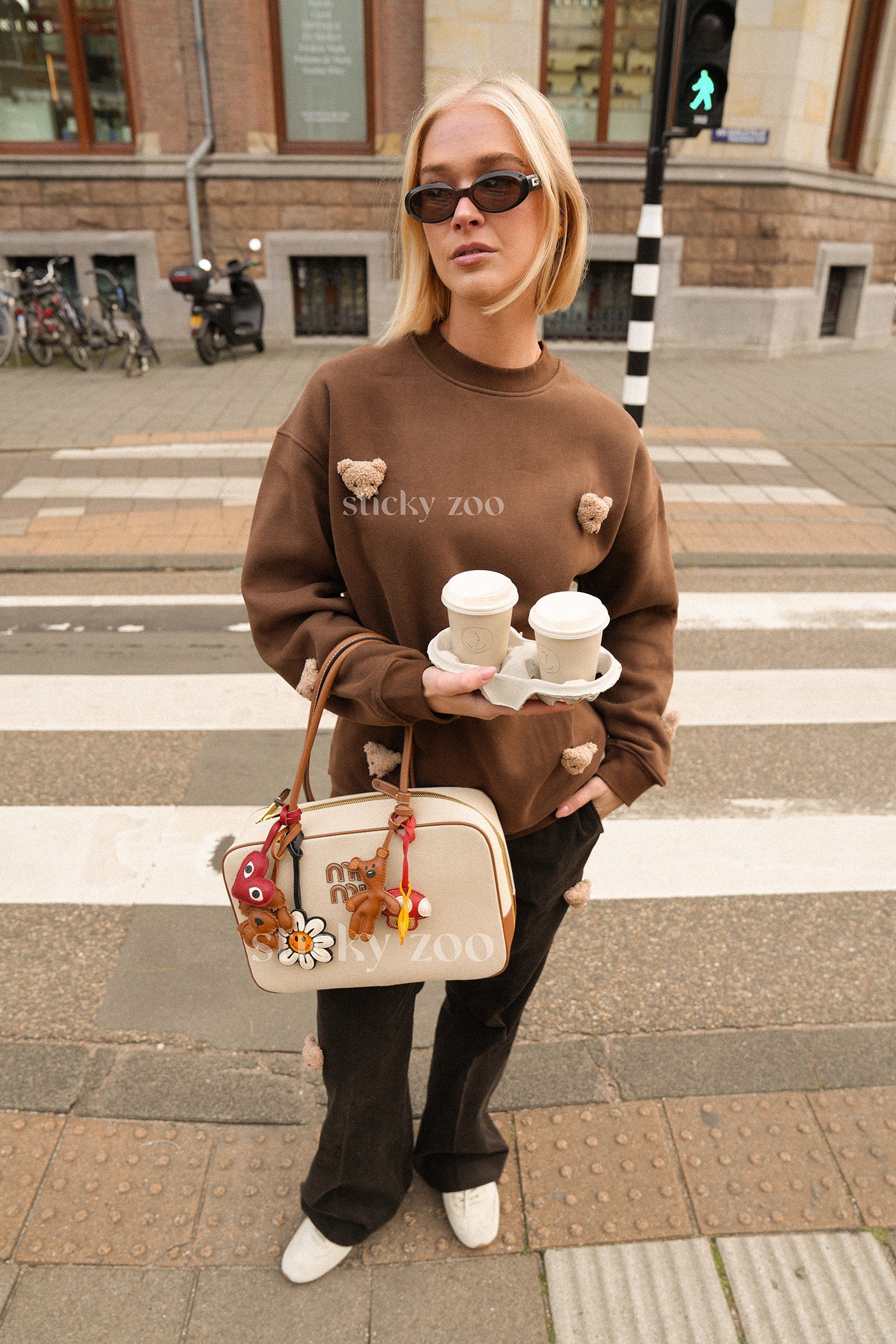Model styled in STICKYZOO brown sweatshirt with six plush bear faces in everyday setting